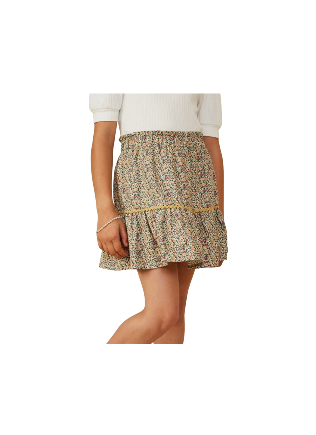 A model wearing a tiered ruffle mini skirt with a dense multicolor floral print in beige, green, and yellow tones, paired with a white ribbed top against a plain white background.