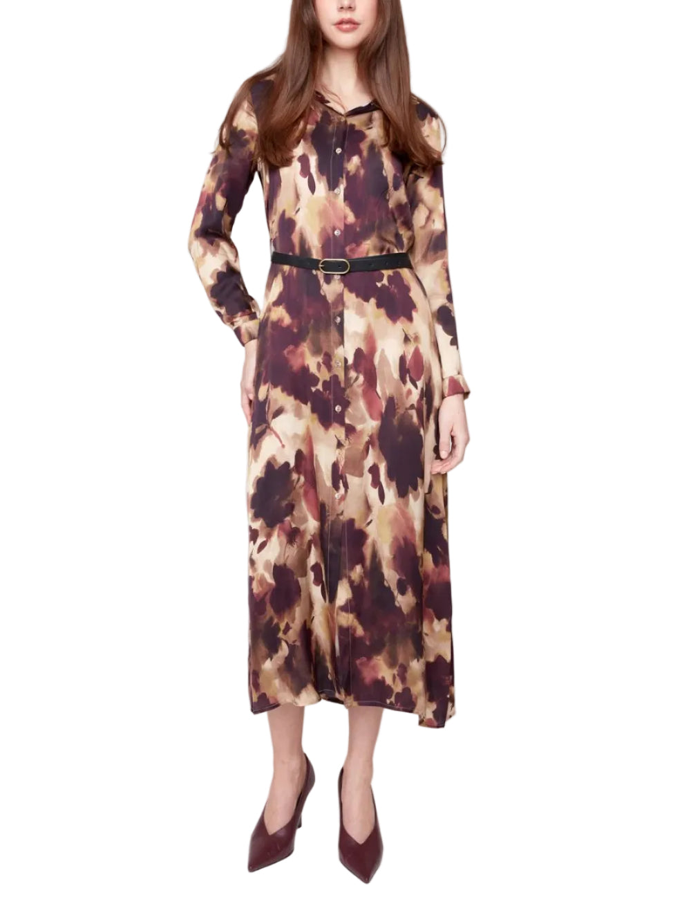 A woman modeling a long-sleeved midi dress with a brown, beige, and black abstract tie-dye pattern, featuring a thin black belt at the waist and paired with dark brown pointed-toe heels, set against a plain light gray studio background.