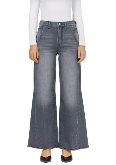 A model wearing a pair of high-waisted, wide-leg denim jeans in a faded gray wash, paired with a white long-sleeve top and black pointed flats, shown against a plain light gray background.