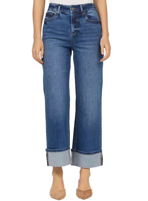 A model wearing a pair of medium-wash blue cropped jeans with rolled cuffs, paired with beige pointed-toe heels, against a plain light gray studio background.