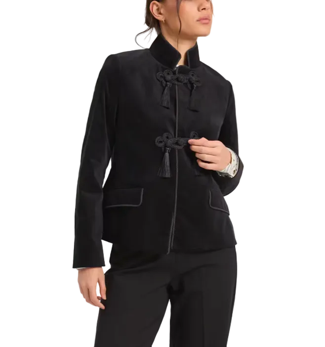 A model wearing a black velvet Chinese-style jacket with decorative tassel and knot frog closures, paired with black trousers, against a plain light gray background.