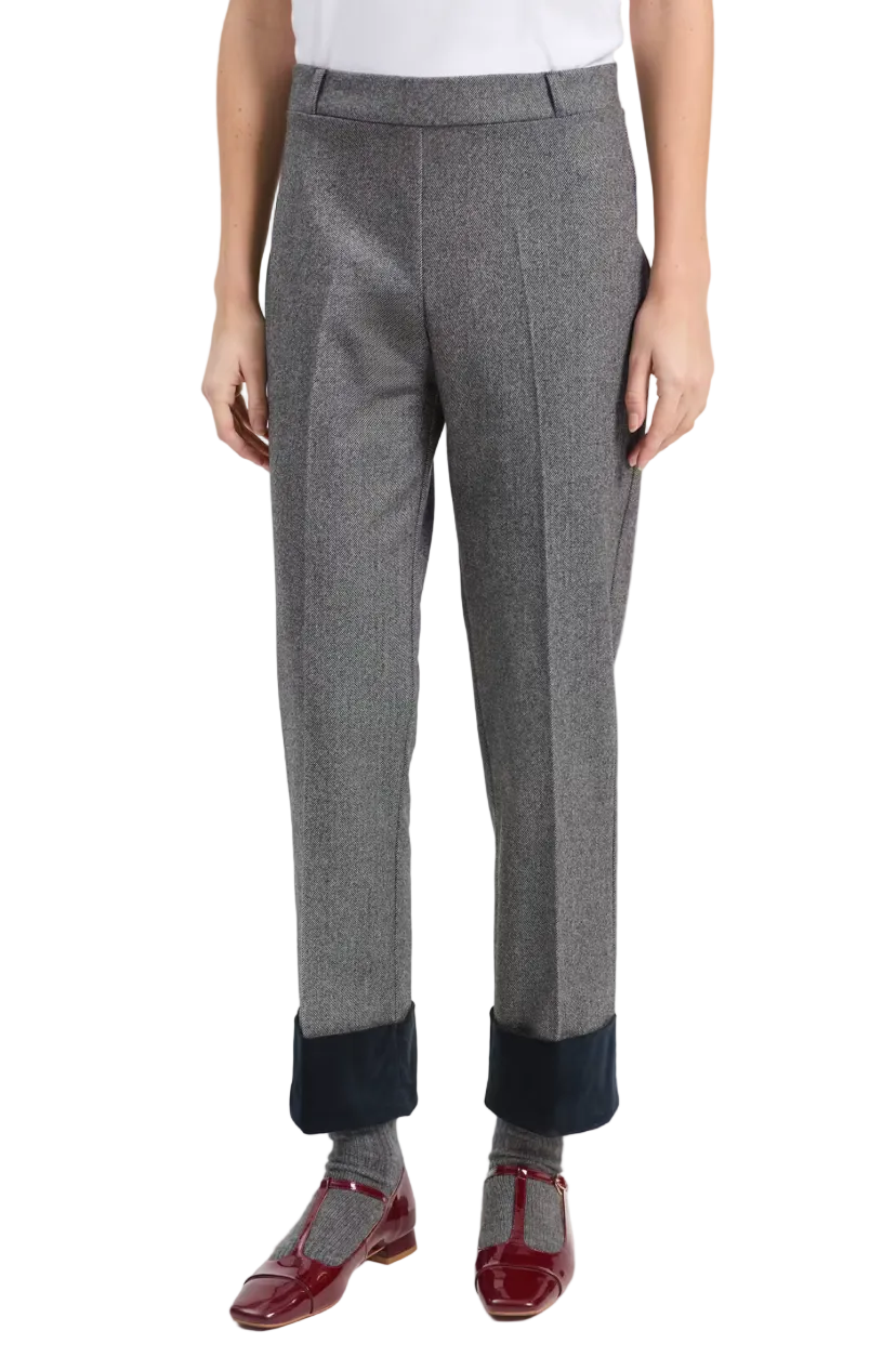 A person wearing gray herringbone trousers with dark navy turned-up cuffs, gray socks, and burgundy Mary Jane shoes, photographed against a light gray studio background.