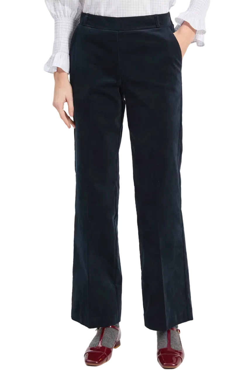A person wearing dark navy wide-leg corduroy trousers, styled with a white gingham blouse and burgundy flat shoes, photographed against a light gray studio background.