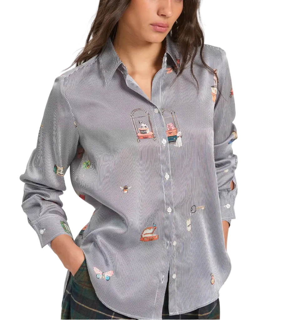 A woman wearing a gray and white striped button-down shirt with colorful embroidered cartoon motifs, paired with a plaid skirt, against a plain light gray background.
