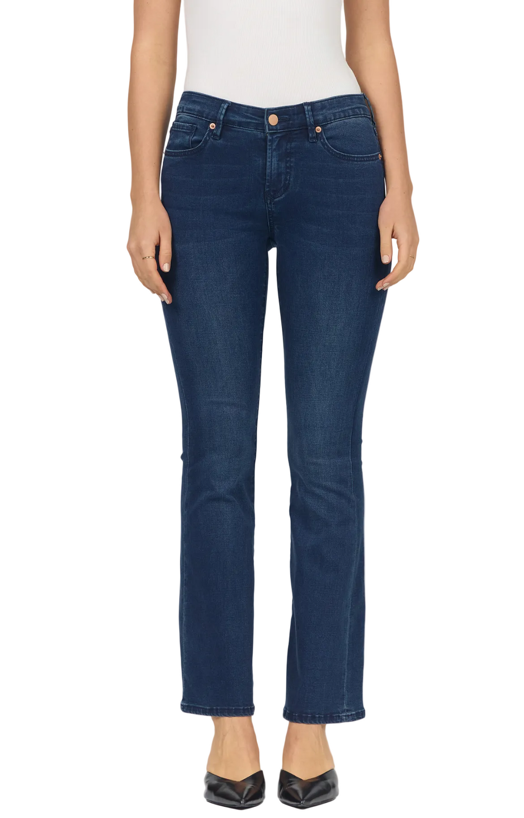 A model wearing a pair of dark blue straight-leg jeans, styled with a white top and black pointed-toe heels, photographed against a light gray studio background.