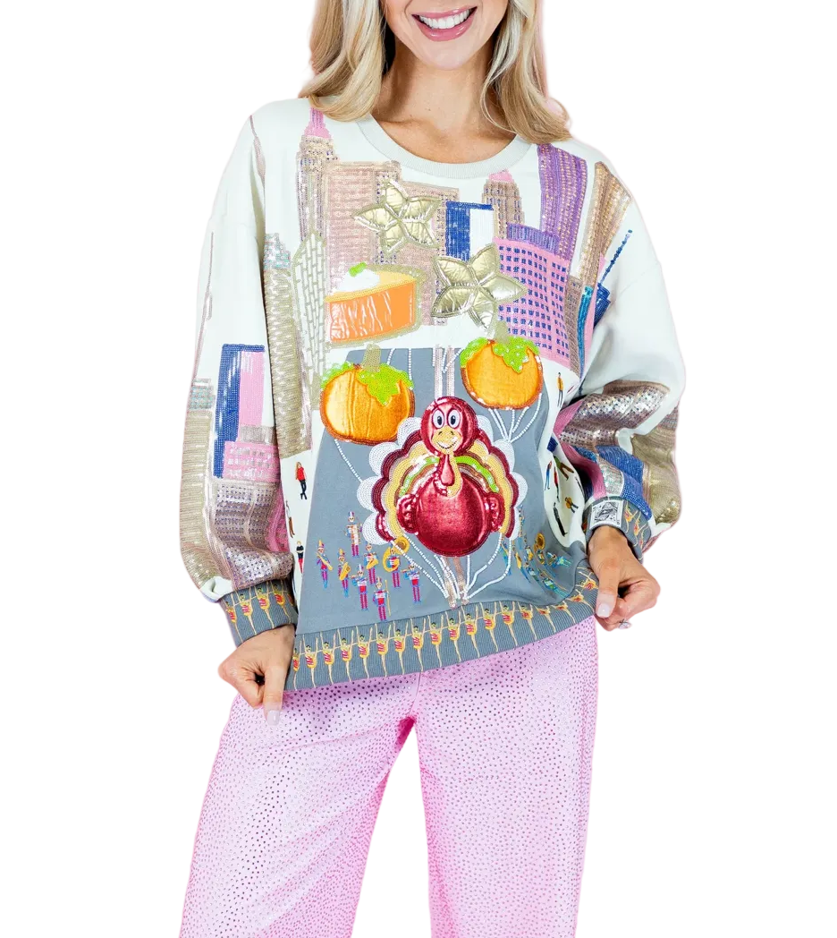 A woman wearing a colorful, patterned crewneck sweatshirt and pink patterned pants, standing against a solid pink studio background.