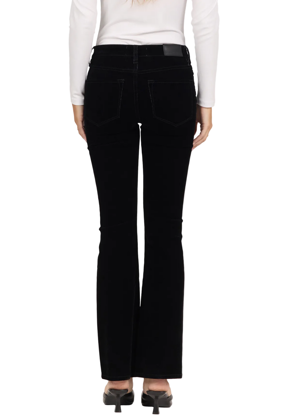 Rear view of a model wearing black flared jeans with a white long-sleeve top and black heels, against a plain white studio background.