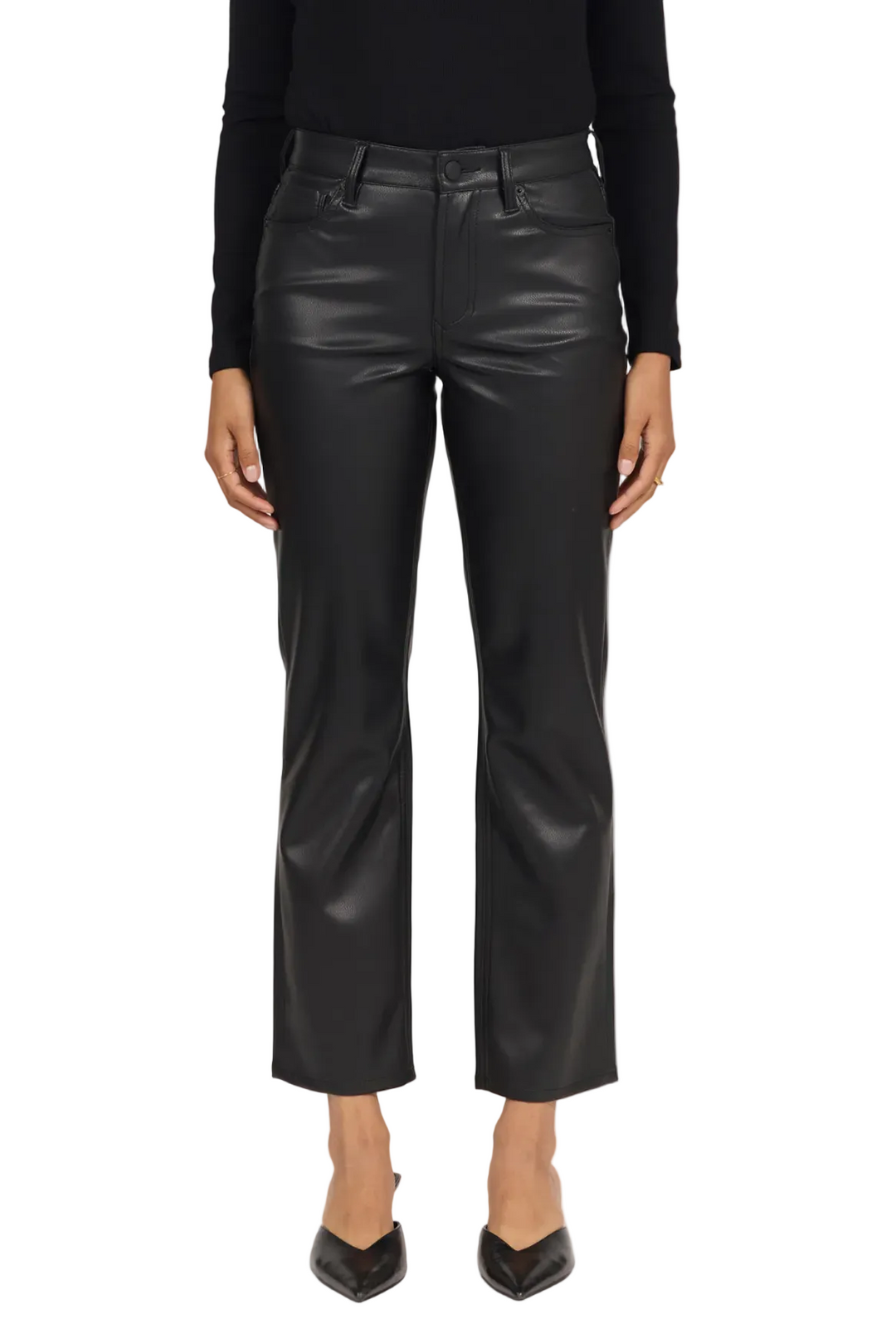 A model wearing black cropped faux-leather trousers with a subtle sheen, paired with a black long-sleeve top and black pointed-toe heels, shown against a plain light gray studio background.