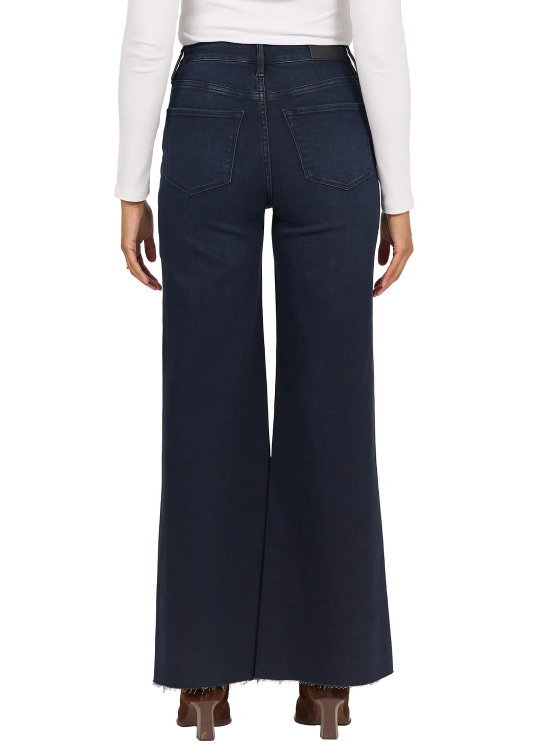 A person shown from the back wearing dark navy wide-leg jeans, a white long-sleeve top, and brown heels against a plain light background.