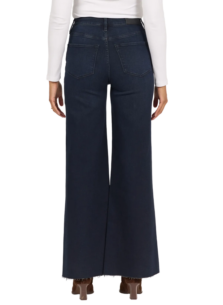 A person shown from the back wearing dark navy wide-leg jeans, a white long-sleeve top, and brown heels against a plain light background.