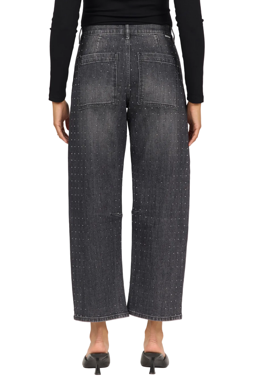 Rear view of a model wearing wide-leg cropped jeans in washed black denim with a subtle dotted pattern, paired with a black long-sleeve top and black pointed mule heels, against a plain light background.