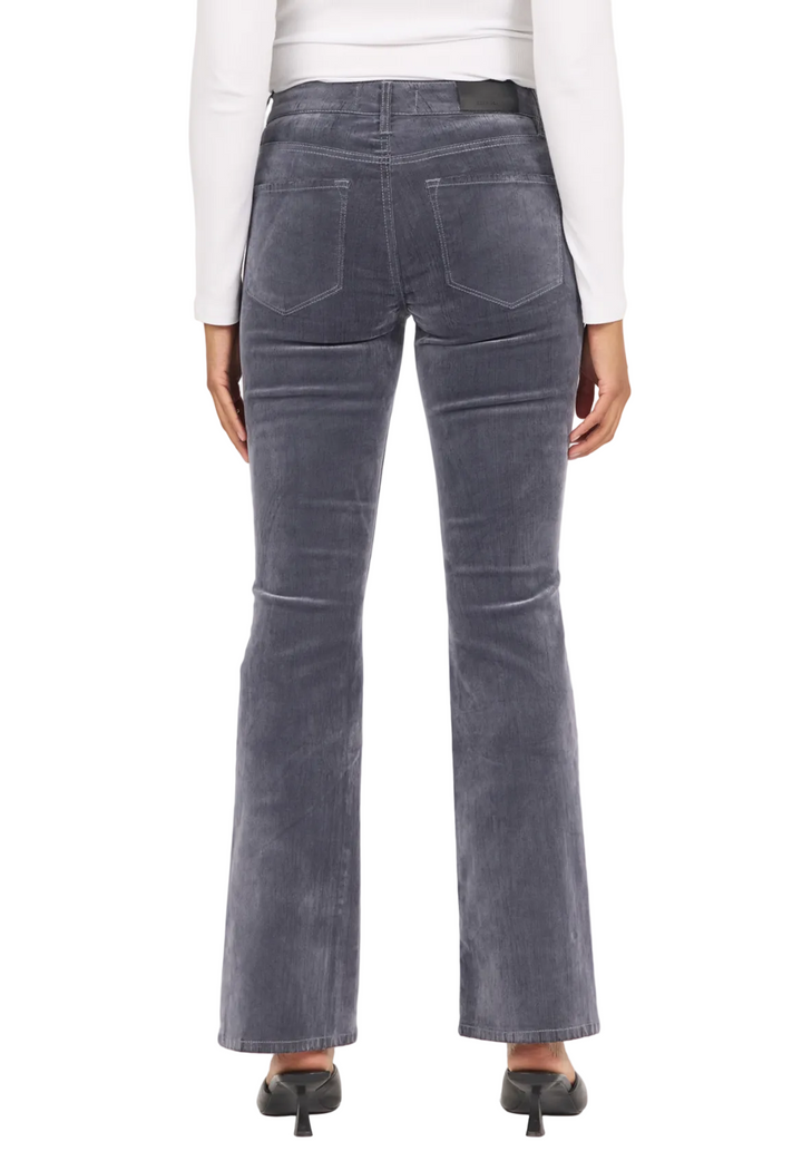 Rear view of a person wearing slate blue flare jeans with a white long-sleeve top and black heels, against a plain light background.