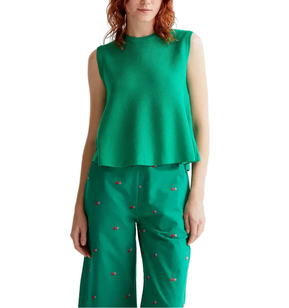 Woman wearing a green sleeveless top and green pants with red patterns on a white background