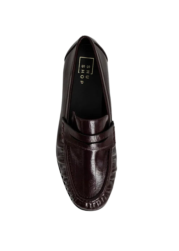 Meet the Tokyo Loafer in a deep wine hue an elevated take on a timeless essential. Crafted in a smooth leather-like material with a polished finish, this style brings a refined pop of color while keeping a classic, structured silhouette. The traditional penny loafer design is enhanced with subtle gathered detailing along the vamp, adding texture and dimension. 