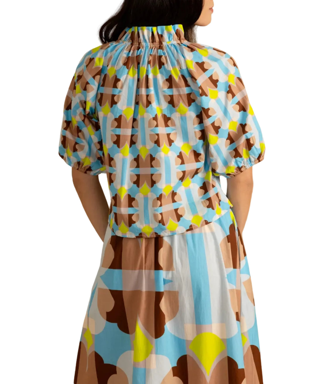 Woman wearing the Trish Top in Small Deco by Double A, a colorful patterned top on a beige background