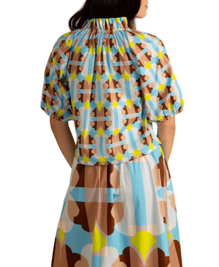 Woman wearing the Trish Top in Small Deco by Double A, a colorful patterned top on a beige background