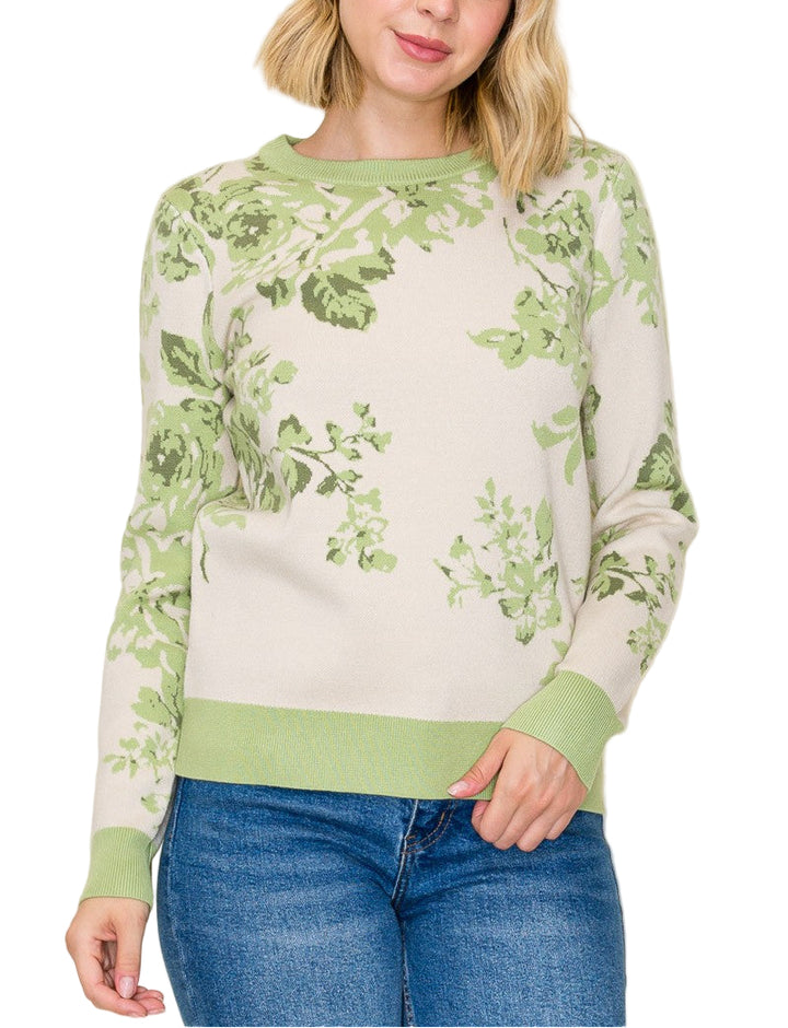 Woman wearing a green and white floral-patterned sweater with blue jeans on a plain background