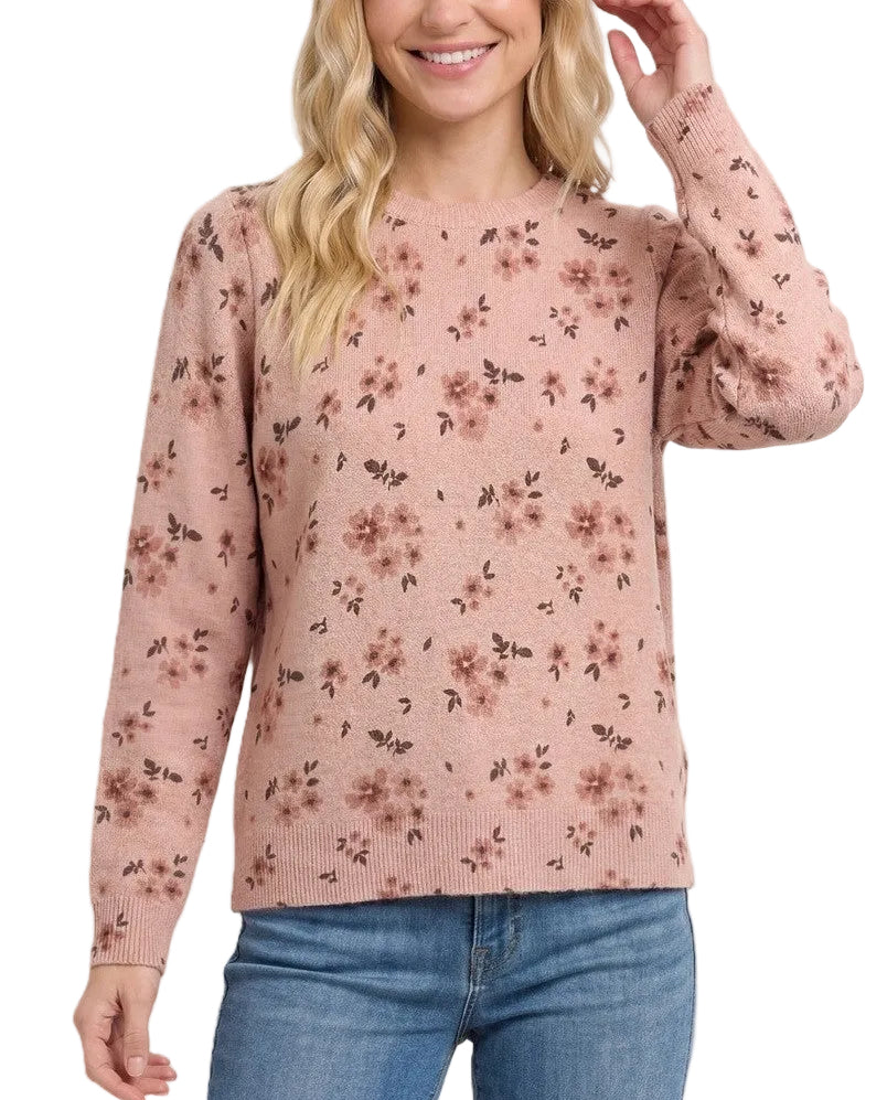 A woman wearing a dusty pink long-sleeve knit sweater with a small dark floral pattern, paired with blue jeans, against a solid light beige background.