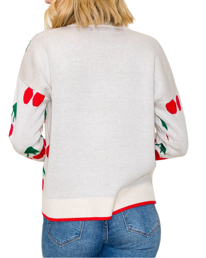 Person wearing a light gray sweater with red and green patterns on sleeves against a plain background