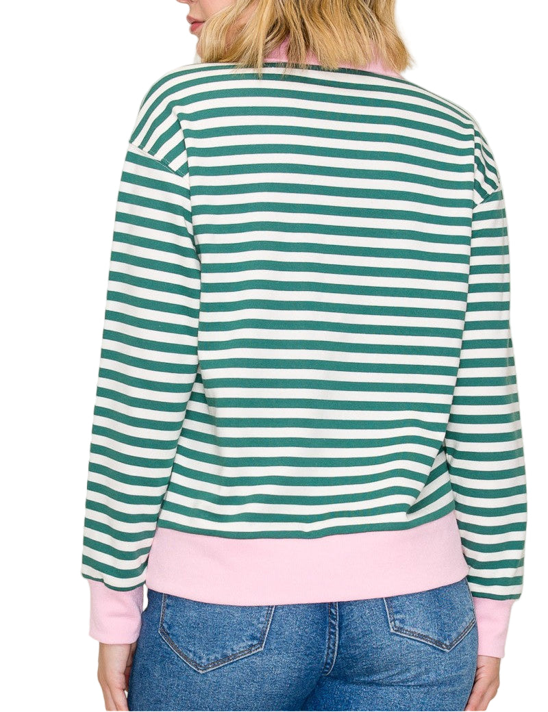 Person wearing a green and white striped sweater with pink trim, standing against a plain background.