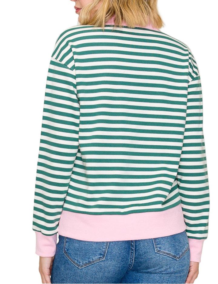 Person wearing a green and white striped sweater with pink trim, standing against a plain background.