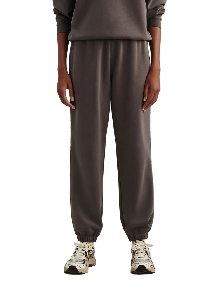 A person wearing dark gray jogger sweatpants with elastic cuffs, paired with a matching gray sweatshirt and white sneakers, shown from the chest down against a plain light gray studio background.