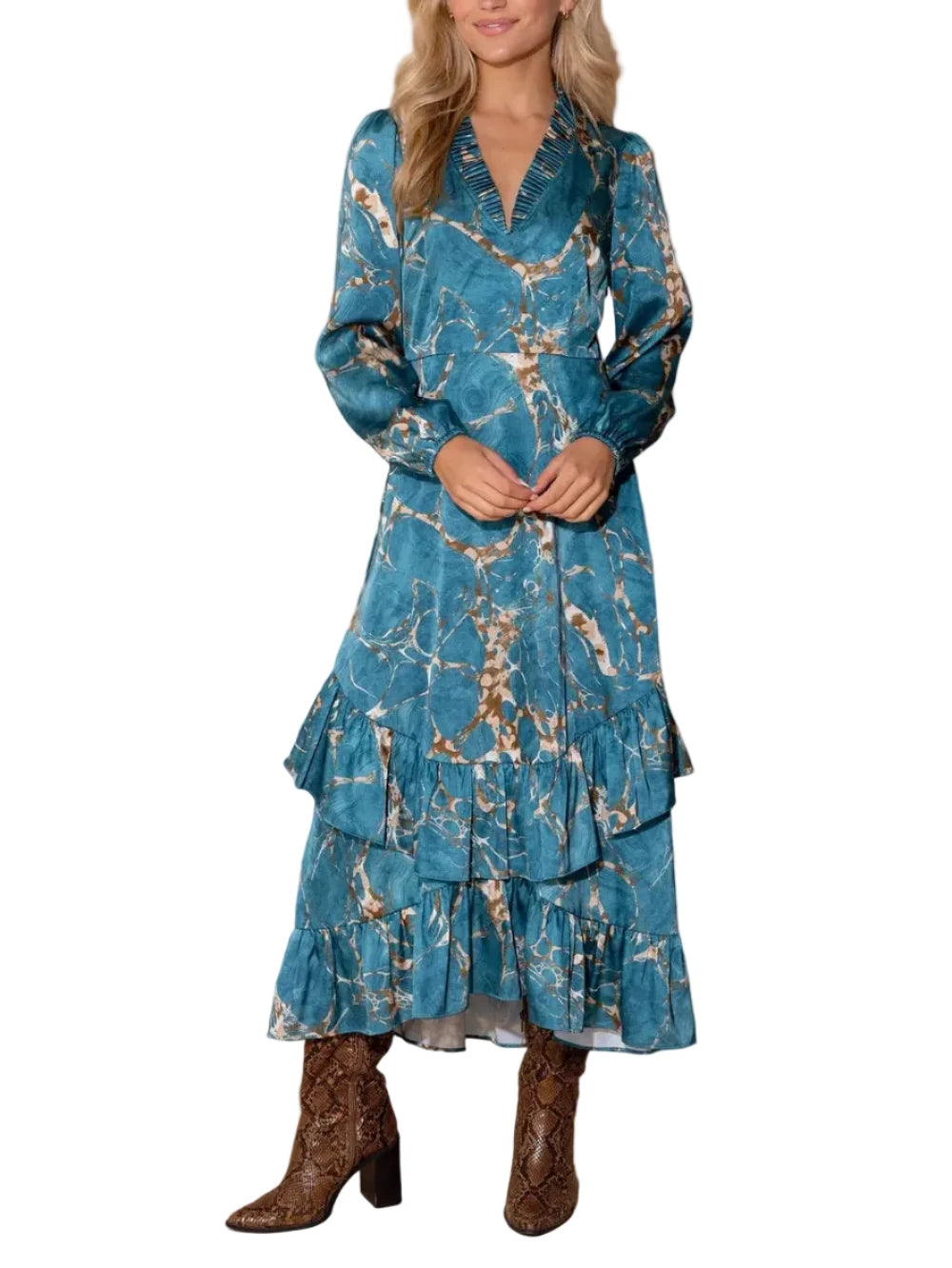 A woman modeling a long-sleeve teal blue maxi dress with a gold and brown abstract marble pattern, paired with brown textured cowboy boots, against a solid white background.