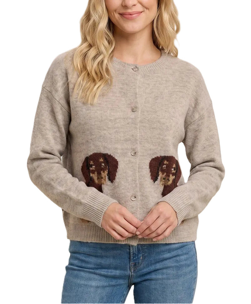 A woman wearing a light beige knit cardigan sweater with two brown dog face patches on the lower front, paired with blue jeans, against a solid light beige background.