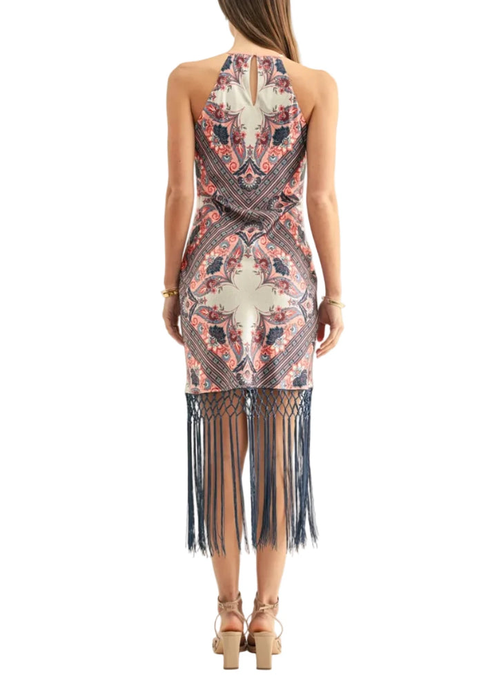 A woman viewed from the back wearing a sleeveless halter-neck dress with a navy, coral, and beige bohemian-style pattern and a long fringe hem, paired with tan strappy heels against a plain white background.