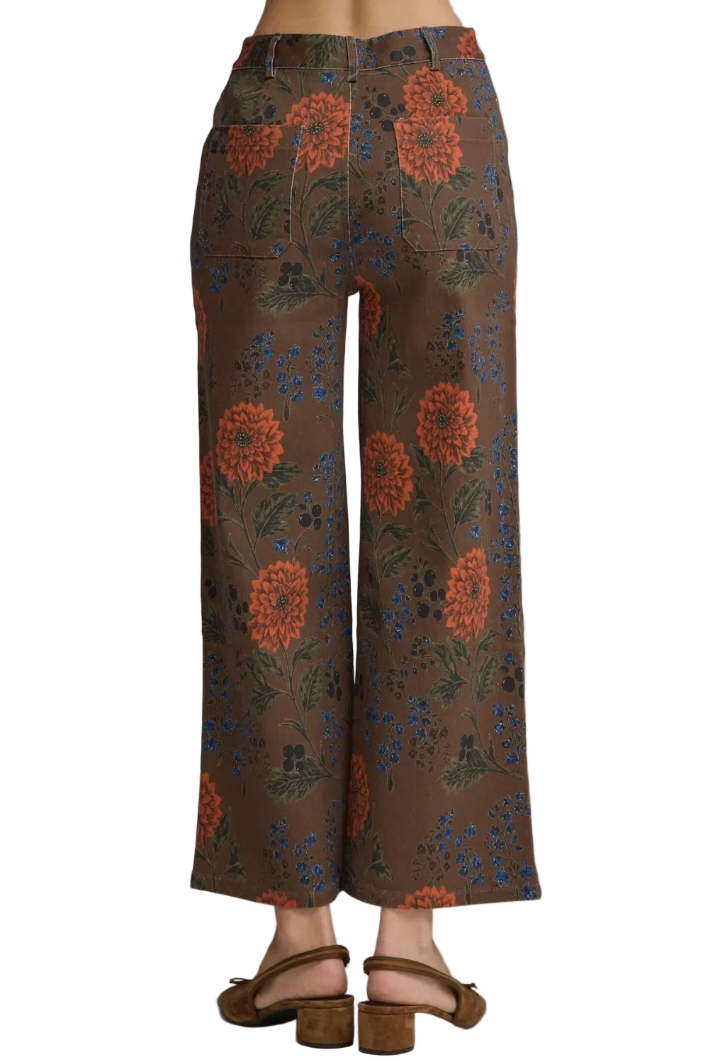 A person shown from the back wearing wide-leg cropped pants with a brown base and an allover floral print in orange, blue, and green, paired with brown flat sandals against a light gray studio background.