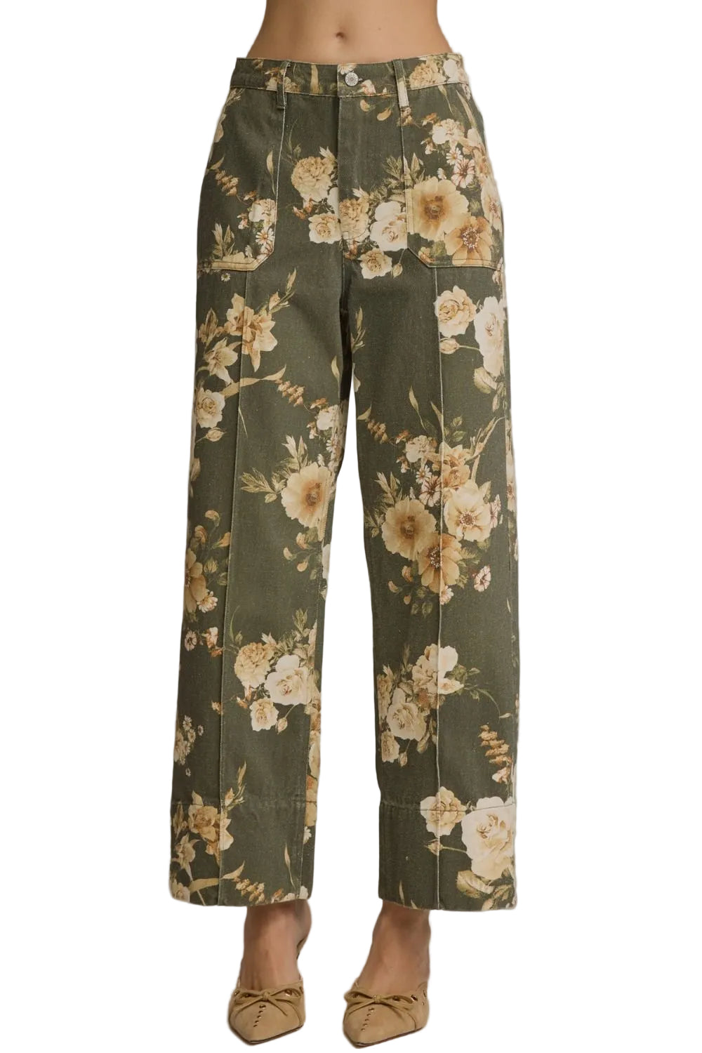 A model is wearing a pair of olive green wide-leg pants with a beige and cream floral print, paired with tan pointed-toe flats, against a solid gray studio background.