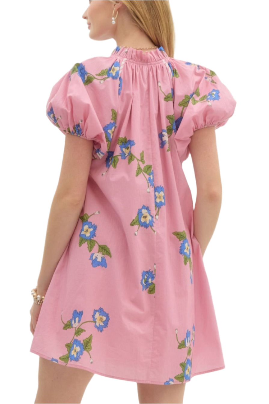 Floral print pullover swing mini dress featuring short puff sleeve accented with contrast seam binding. Pockets at side. Front button closure. Lined. Woven. Non-sheer. Lightweight.