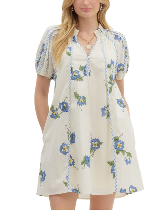 Floral print pullover swing mini dress featuring short puff sleeve accented with contrast seam binding. Pockets at side. Front button closure. Lined. Woven. Non-sheer. Lightweight.