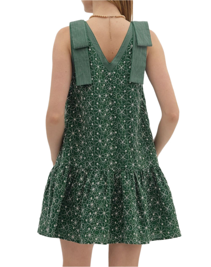 Floral embroidered sleeveless ruffle hem mini dress featuring exposed stitch detail shoulder bow detail and neck. Pockets at sides. Lined. Woven. Non-sheer. Lightweight.