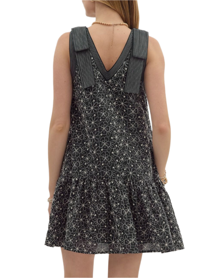 Floral embroidered sleeveless ruffle hem mini dress featuring exposed stitch detail shoulder bow detail and neck. Pockets at sides. Lined. Woven. Non-sheer. Lightweight.