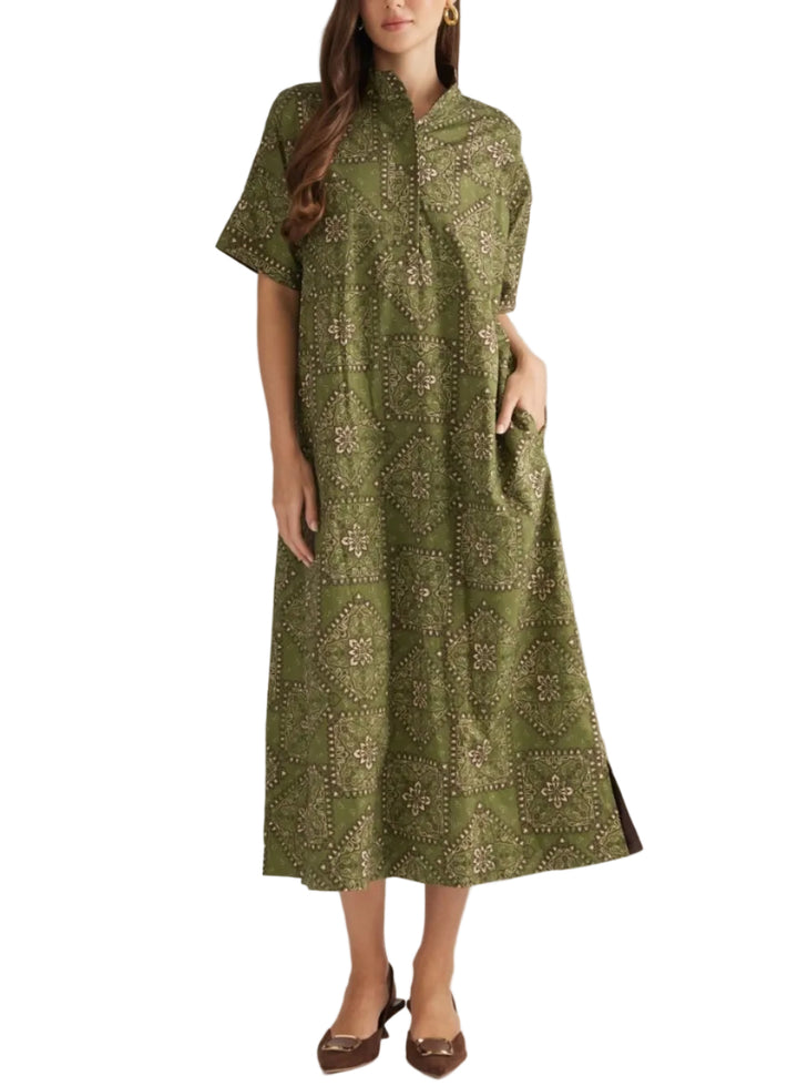 A woman modeling a short-sleeved olive green midi dress with a beige and brown geometric pattern, standing against a plain light gray studio background.