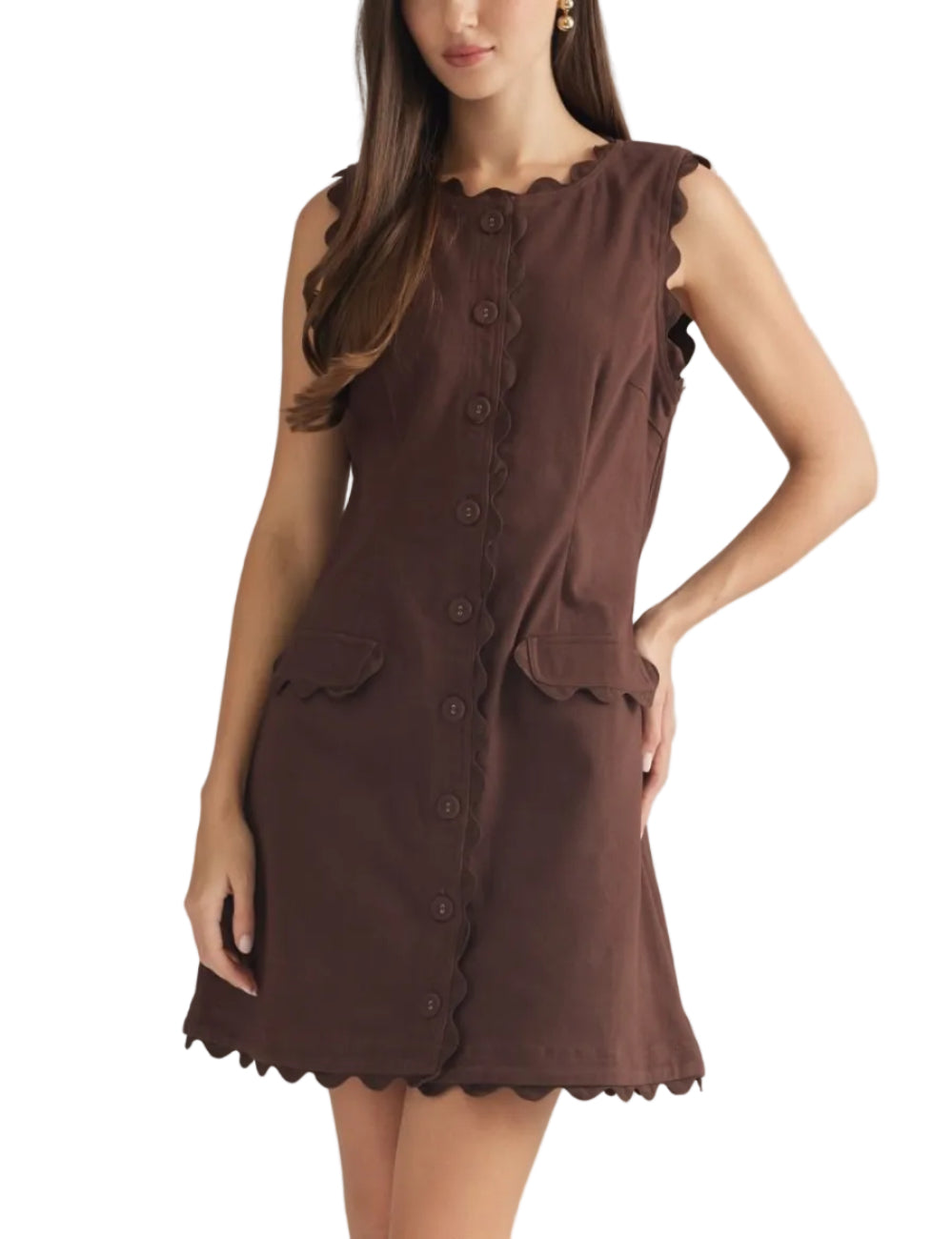 A woman modeling a sleeveless brown dress with scalloped edges, a button-front neckline, and front patch pockets against a plain light gray studio background.