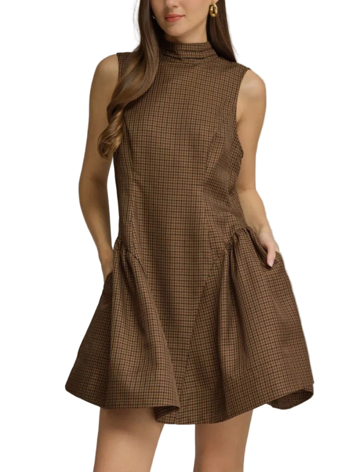 A woman modeling a sleeveless brown mini dress with a high mock neck and a subtle brown-and-black check pattern, set against a solid gray studio background.