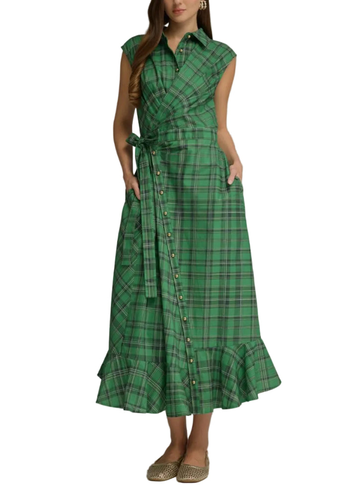 A woman modeling a green plaid midi dress with a wrap-style front, button details, side pockets, and a tie belt, photographed against a neutral gray studio background.