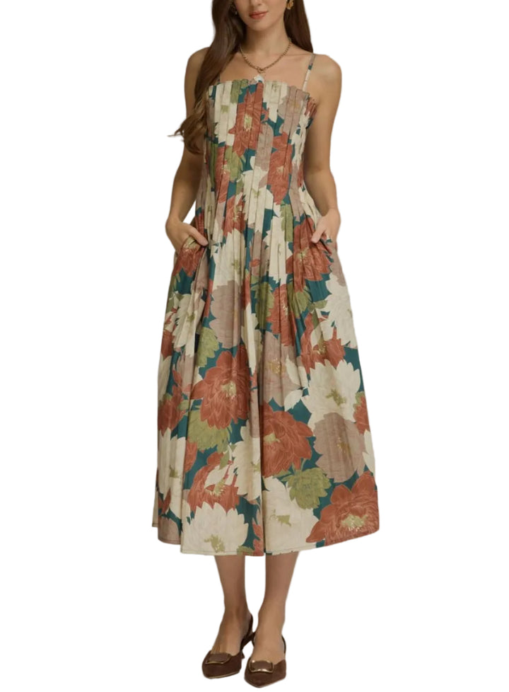 A woman modeling a sleeveless midi dress with a large floral print in beige, rust orange, teal green, and cream, set against a plain gray studio background.