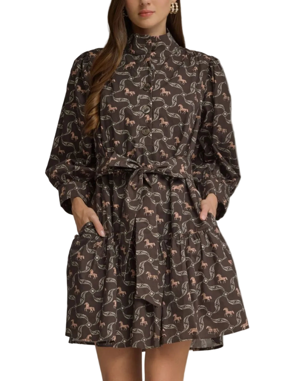 A woman modeling a dark brown long-sleeve mini dress with a high mock neck, puff sleeves, a matching waist tie, and pockets. The dress features an all-over repeating pattern of small pink horses and white abstract swirls, set against a solid gray studio background.