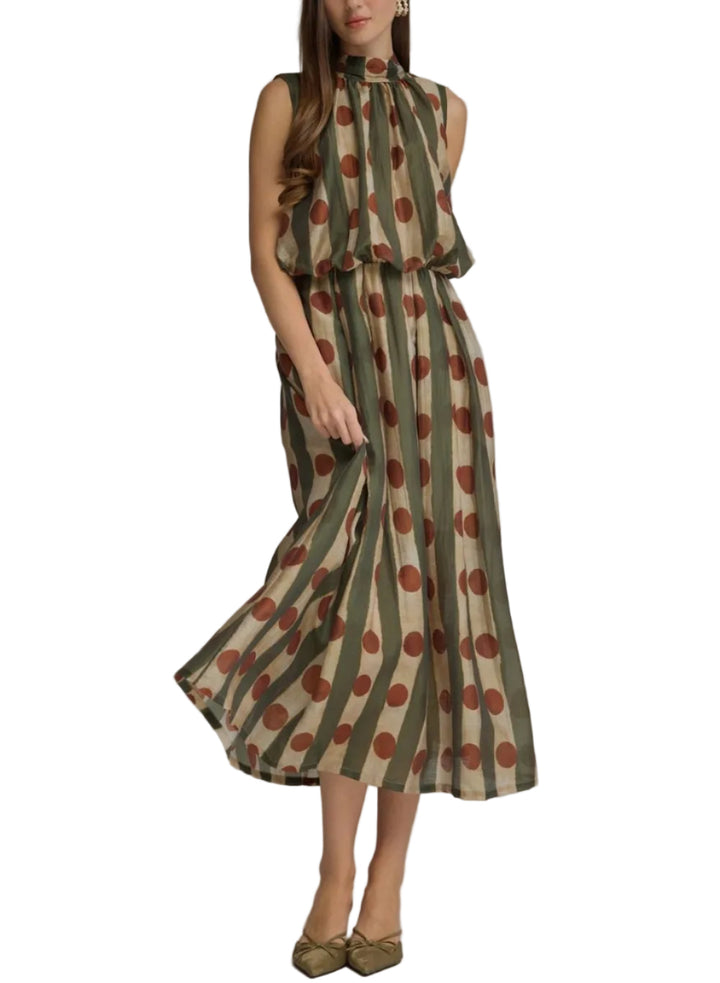 A woman models a sleeveless midi dress with a high ruffled collar, featuring a vertical olive green and beige stripe pattern with large brown polka dots, paired with olive green pointed flats against a neutral gray studio background.