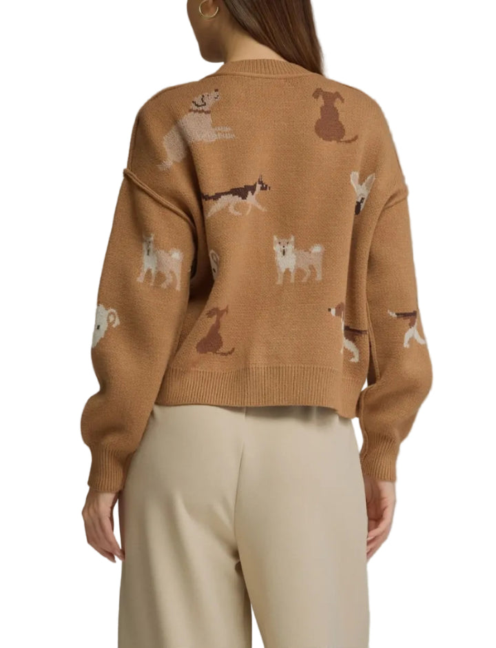A woman shown from the back wearing a cropped tan knit sweater with an allover dog print and light beige trousers, photographed against a plain gray studio background.