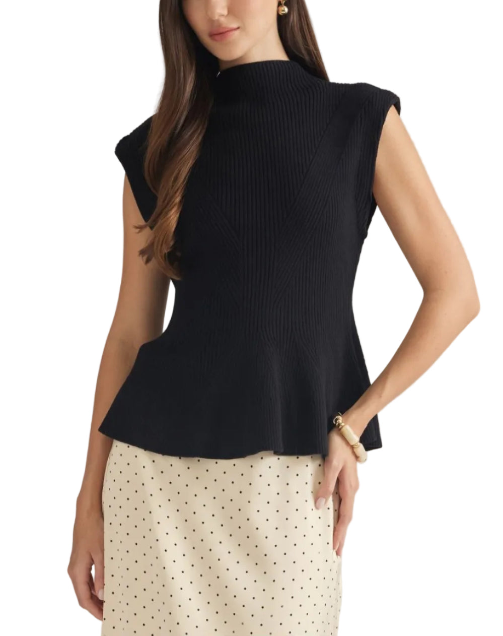 A woman modeling a sleeveless black ribbed mock-neck top with a peplum hem, paired with a cream polka-dot skirt, against a solid light gray background.