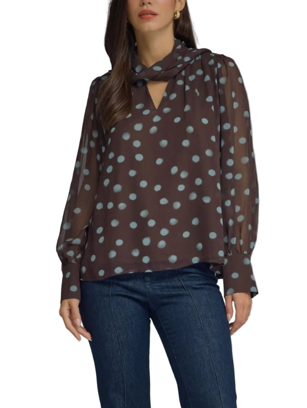 A woman modeling a sheer brown long-sleeve blouse with a light blue polka dot pattern and a keyhole tie neckline, paired with dark blue jeans against a solid gray studio background.