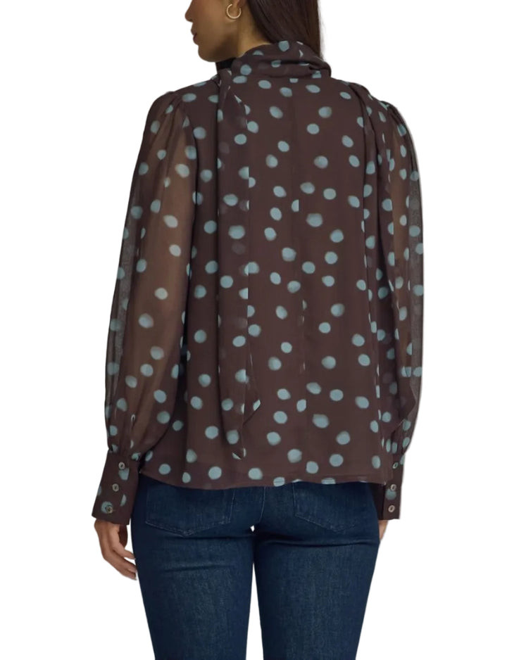 A woman shown from the back wearing a sheer brown long-sleeve blouse with a light blue polka dot pattern and dark blue jeans, photographed against a plain gray studio background.