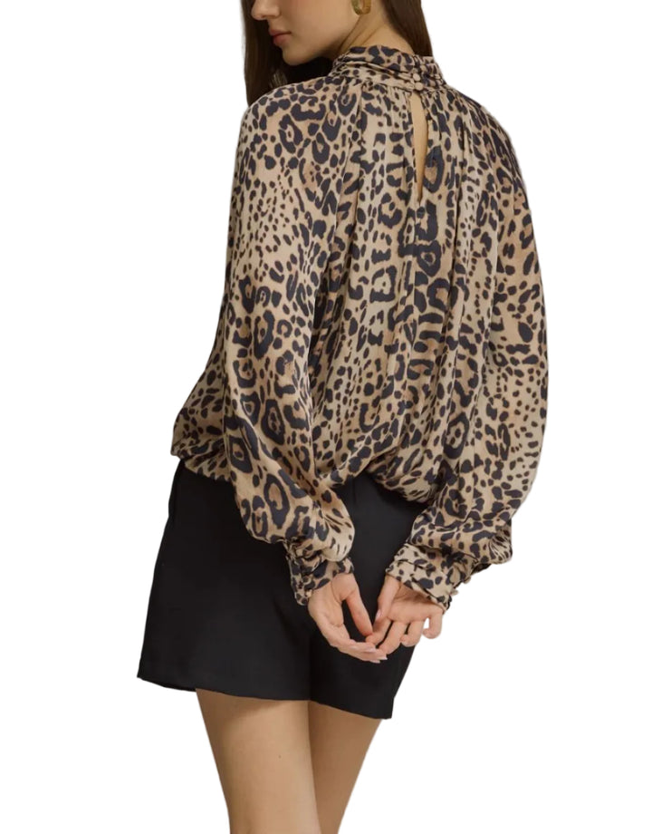 A woman wearing a beige and black leopard print blouse with long balloon sleeves, shown from the back against a plain gray studio background.