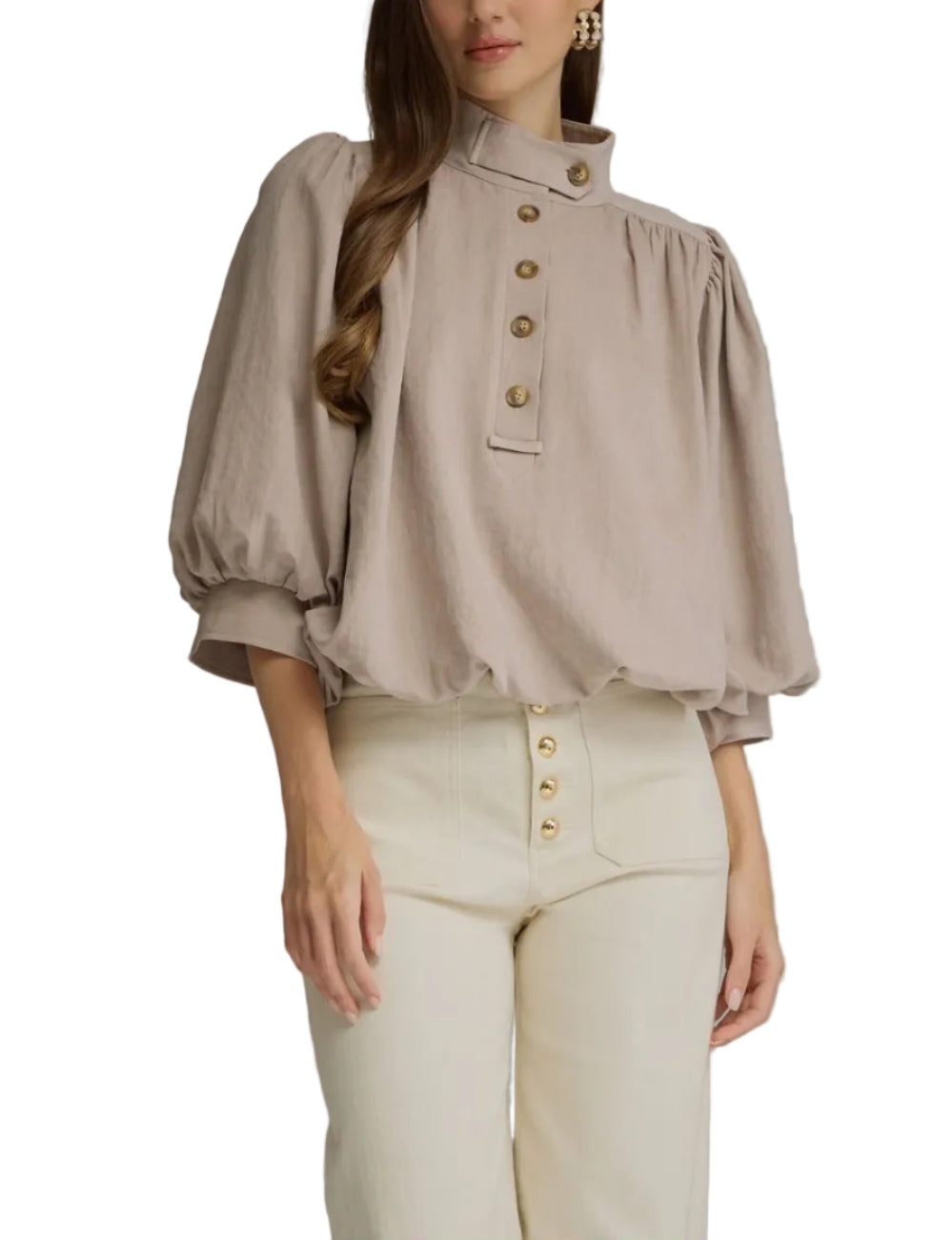 A woman modeling a taupe puff-sleeve blouse with gold-tone buttons down the front, paired with cream pants, against a solid gray studio background.