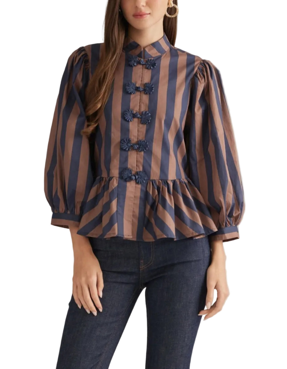 A woman modeling a brown and navy blue vertically striped blouse with 3D floral button details down the front, paired with dark blue jeans, against a solid light beige background.