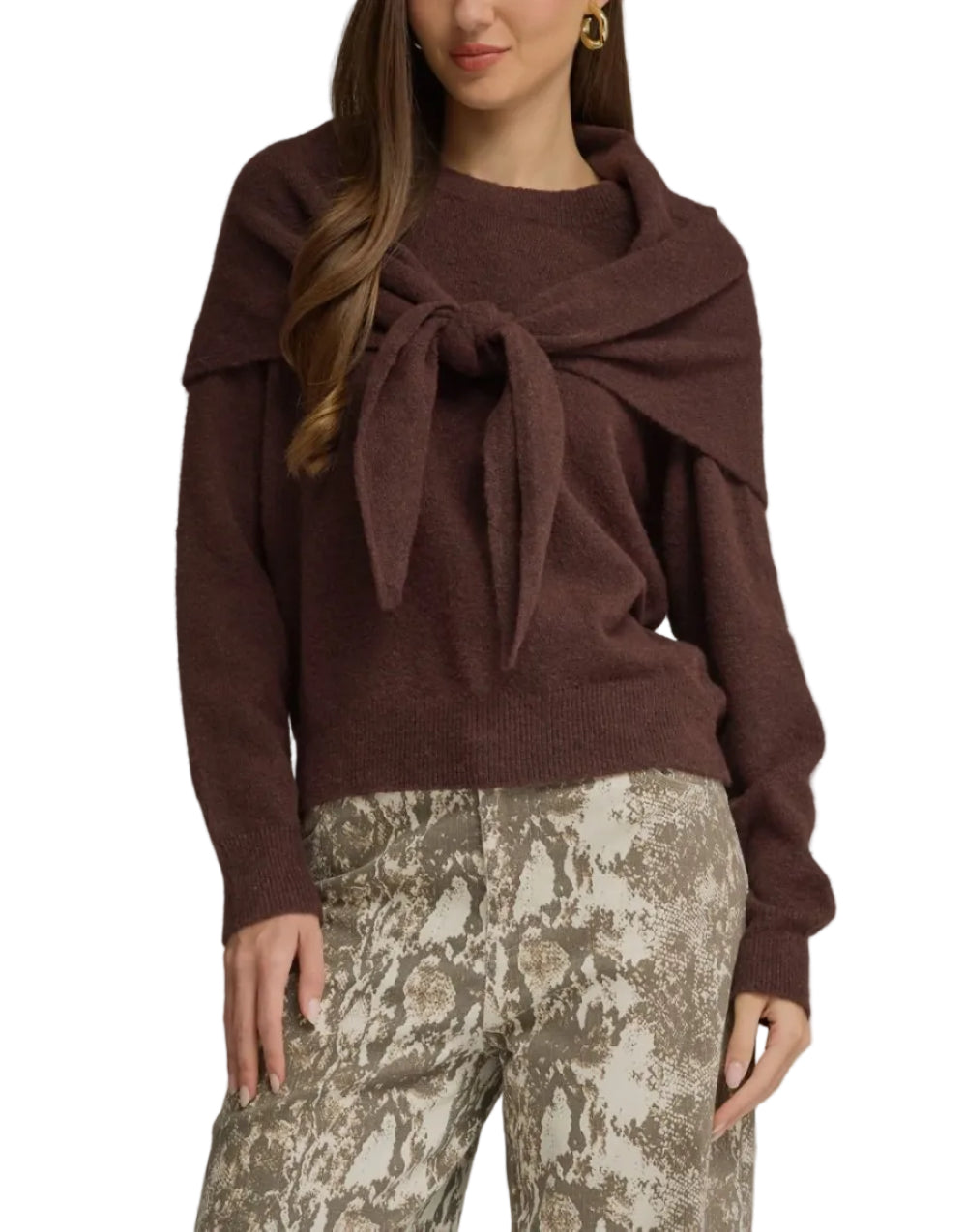 A woman modeling a dark brown knit sweater with a draped collar and front tie detail, paired with beige and brown patterned pants, against a solid gray studio background.